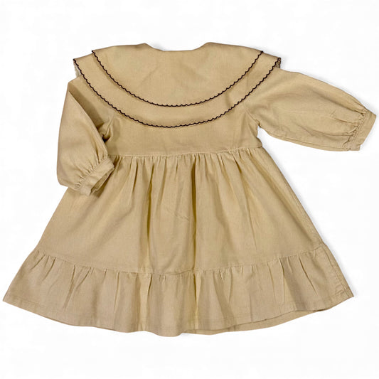 A beige needle-cord children’s dress with oversized Peter Pan bib collar, contrast scalloped trim, long balloon sleeves with gathered cuffs, empire line and full gathered frill hemmed skirt — back view.