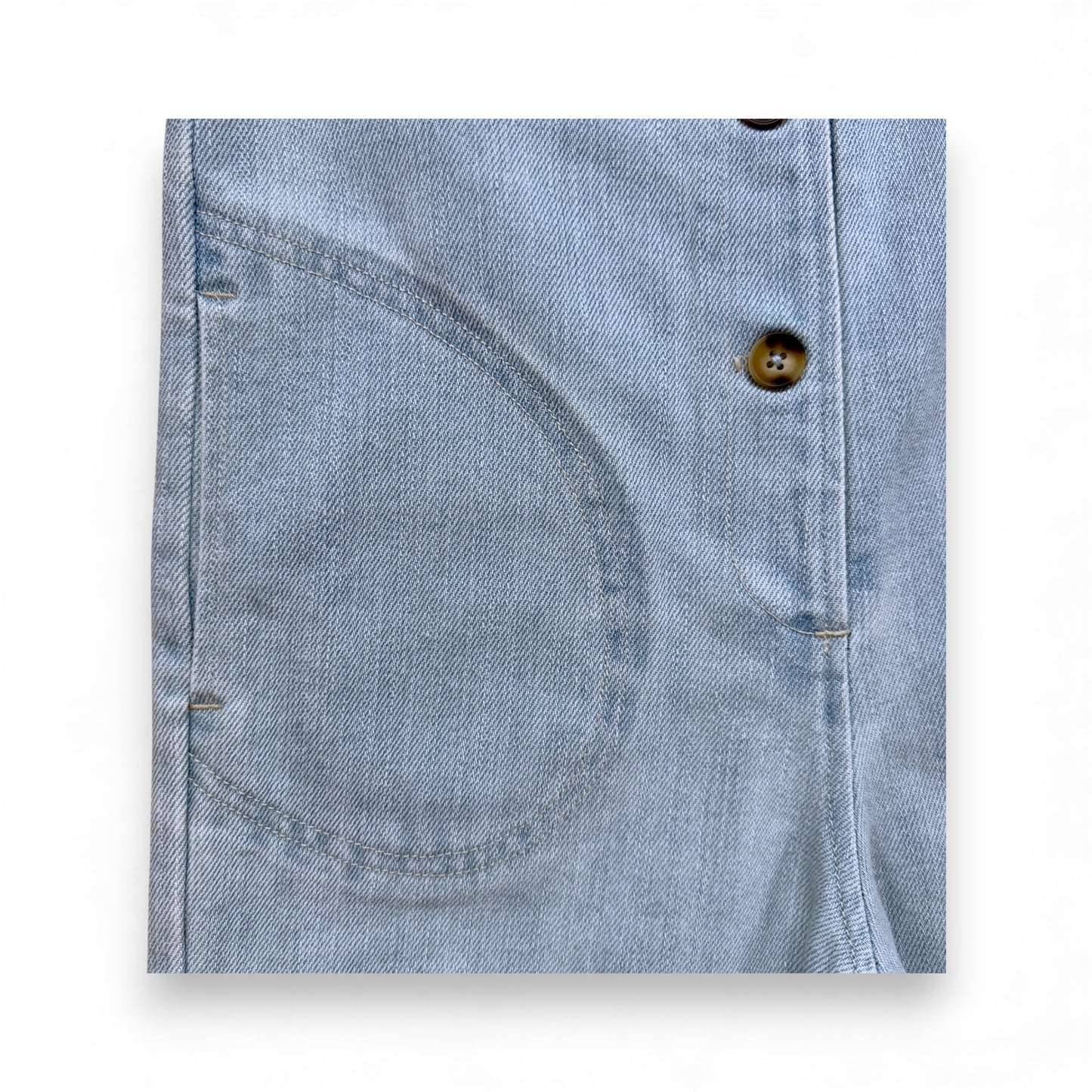 Light blue denim children’s romper with scoop neckline, circular front pockets and full front button closure