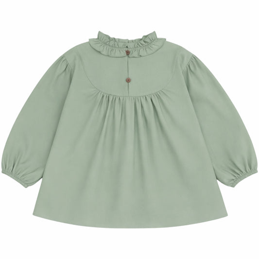 A sage green long-sleeve blouse for toddlers, featuring a ruffled mock neck collar, a gathered empire waist, and elasticized cuffs, shown against a plain white background.
