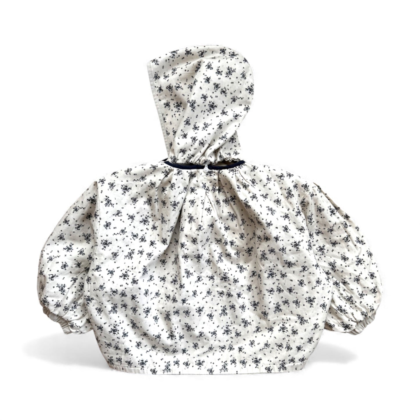 Reversible children’s jacket in floral & cream organic cotton with cream lining, detachable hood, raglan sleeves and circular pockets — back view.