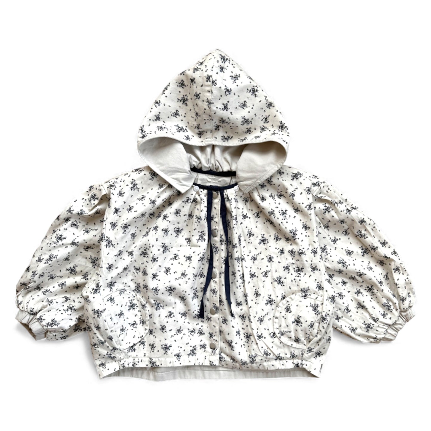 Reversible children’s jacket with Victorian-style floral print, detachable hood, contrast ties, raglan sleeves and circular flap pockets — front view.