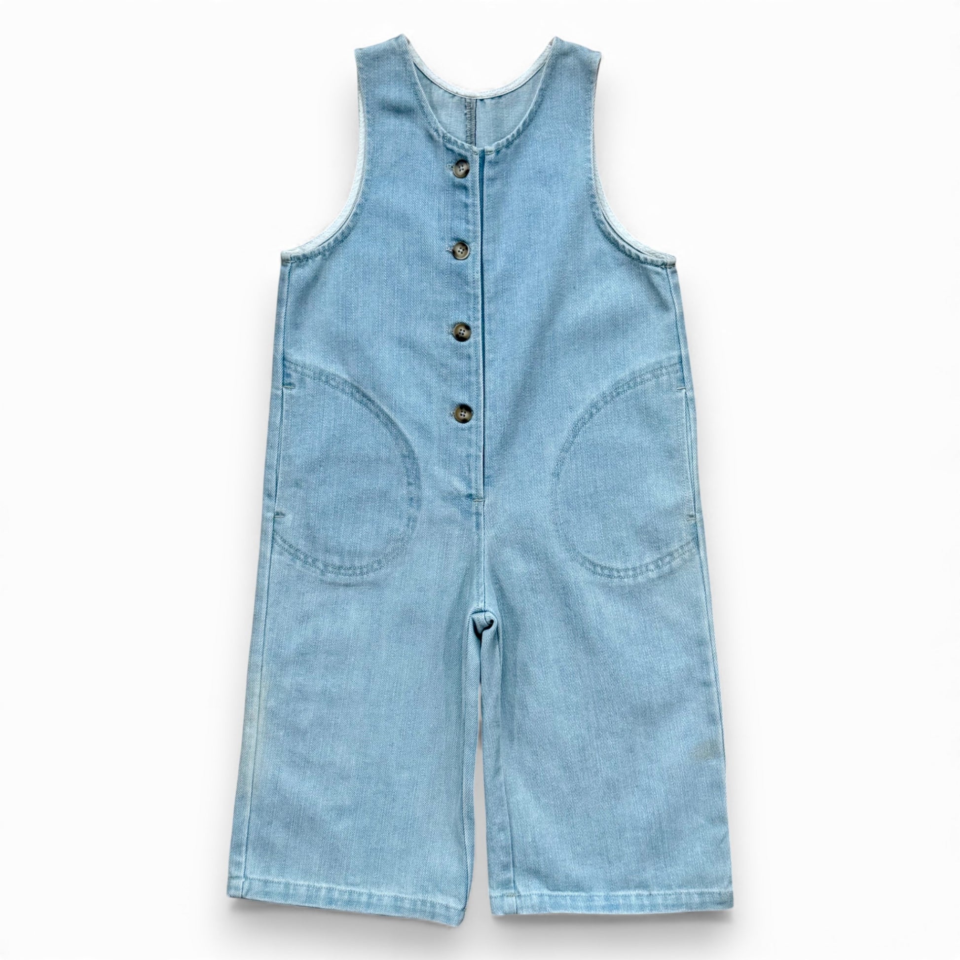 Light blue denim children’s romper with scoop neckline, circular front pockets and full front button closure
