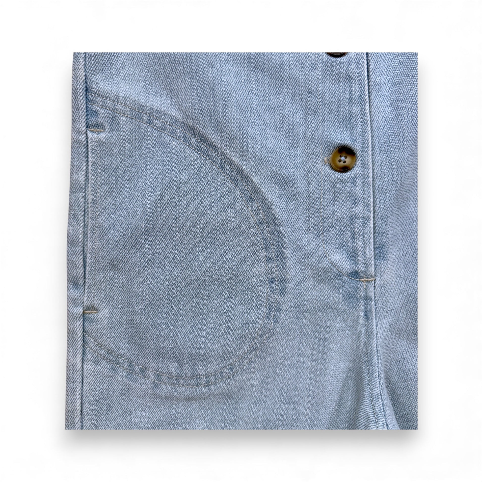 Light blue denim children’s romper with scoop neckline, circular front pockets and full front button closure