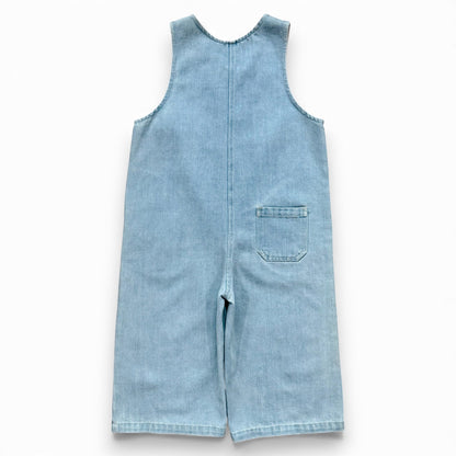 Light blue denim children’s romper with scoop neckline, circular front pockets and full front button closure