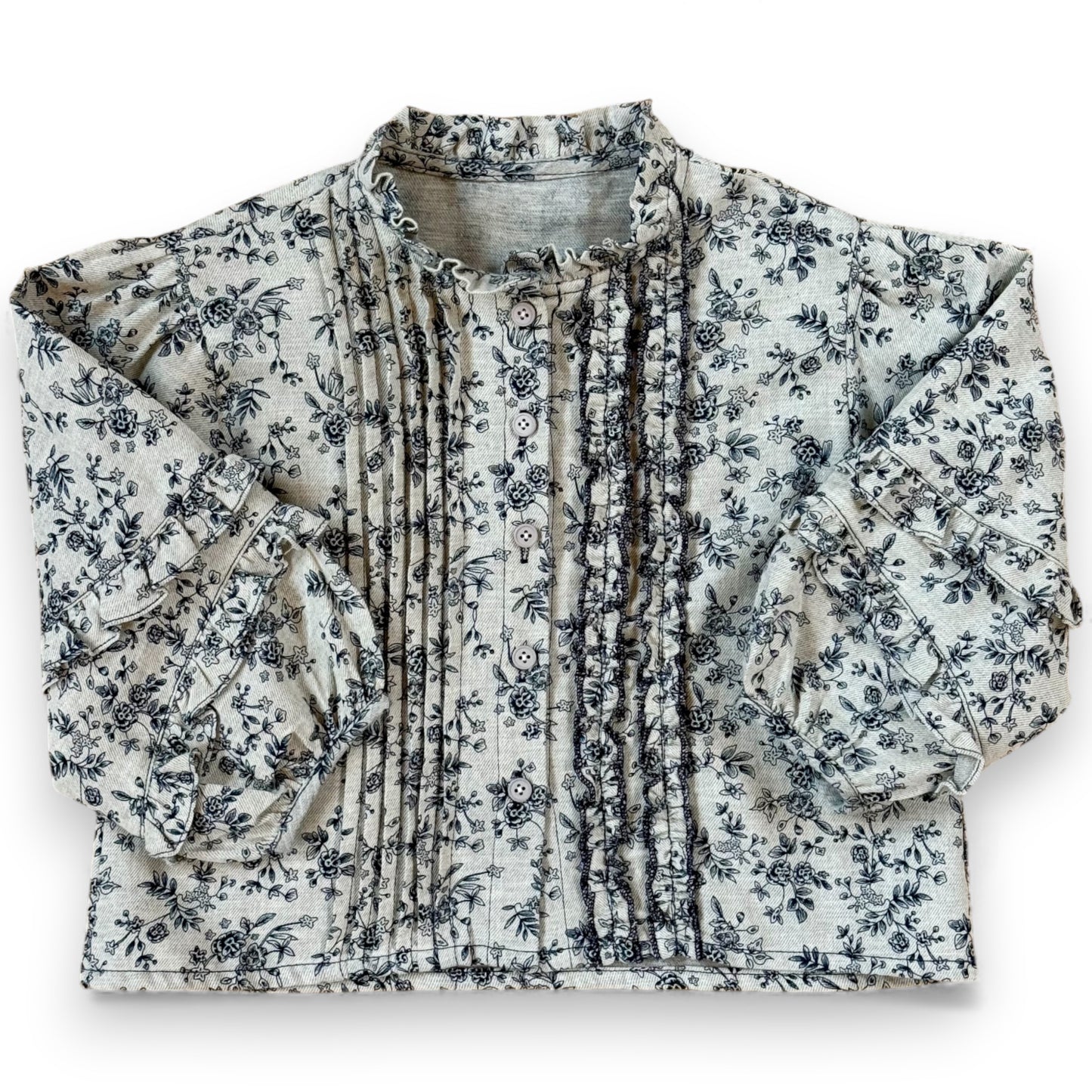 Children’s brushed cotton floral blouse with frilled high neck, front pleats and ruffle detailing, laid flat on cork background