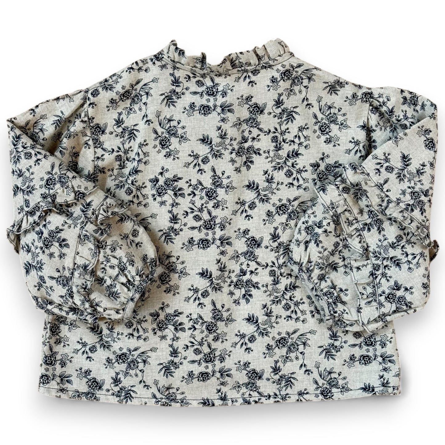 Back view of children’s floral brushed cotton blouse with balloon sleeves and frill seams, laid flat on cork background