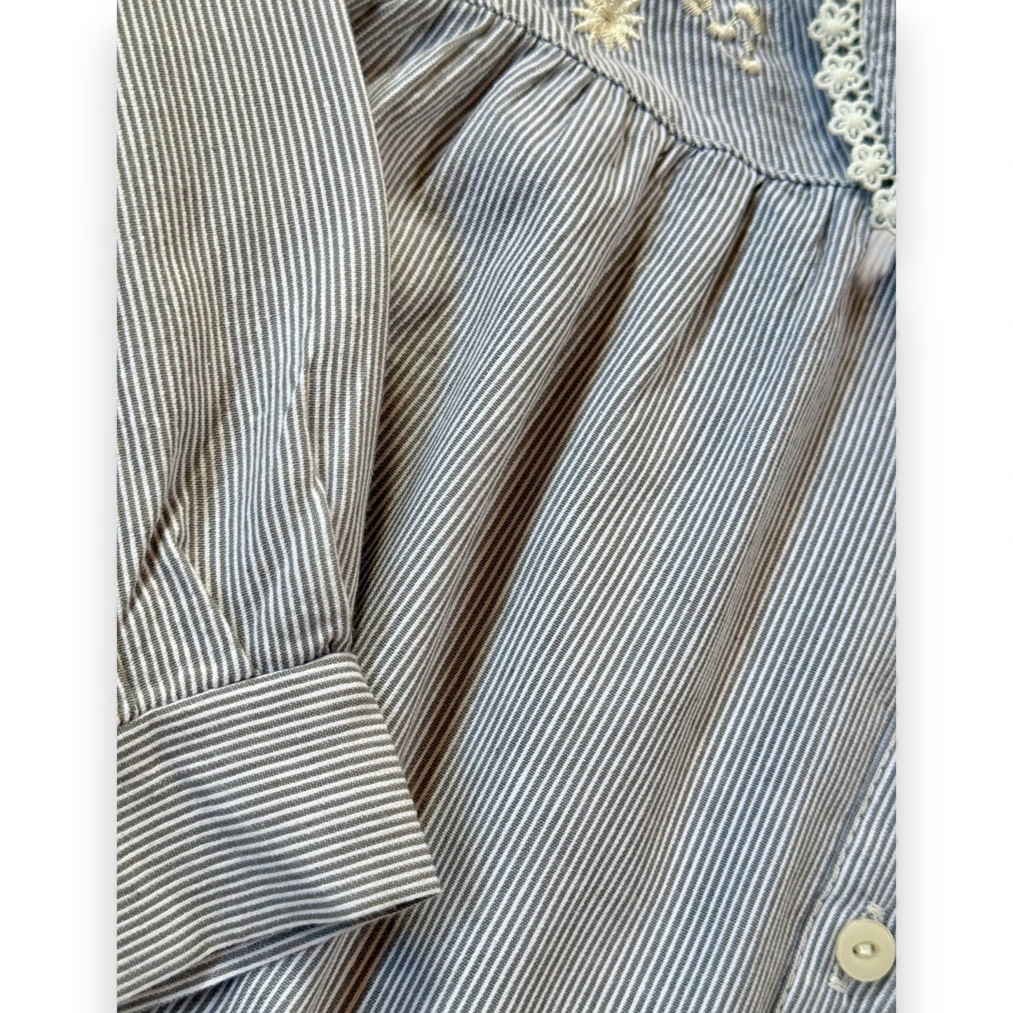 Close-up of pinstripe children’s blouse showing embroidery, lace-trimmed collar and pleat detailing.