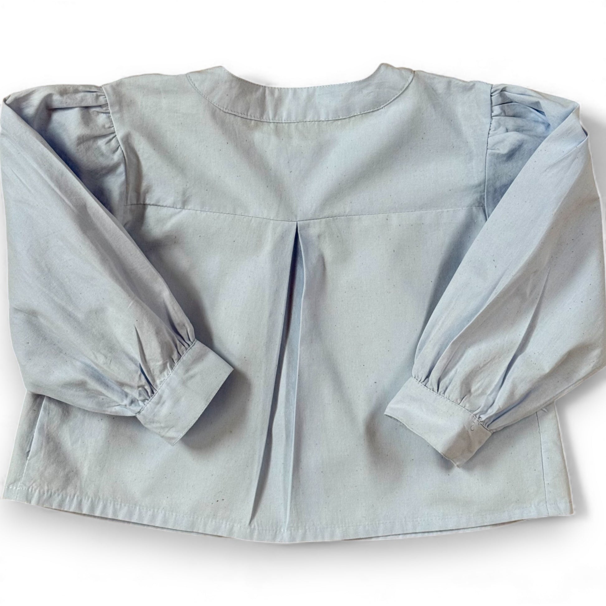 Back view of children’s blue A-line blouse with centre back pleat and gathered sleeves, laid flat.