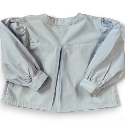 Back view of children’s blue A-line blouse with centre back pleat and gathered sleeves, laid flat.