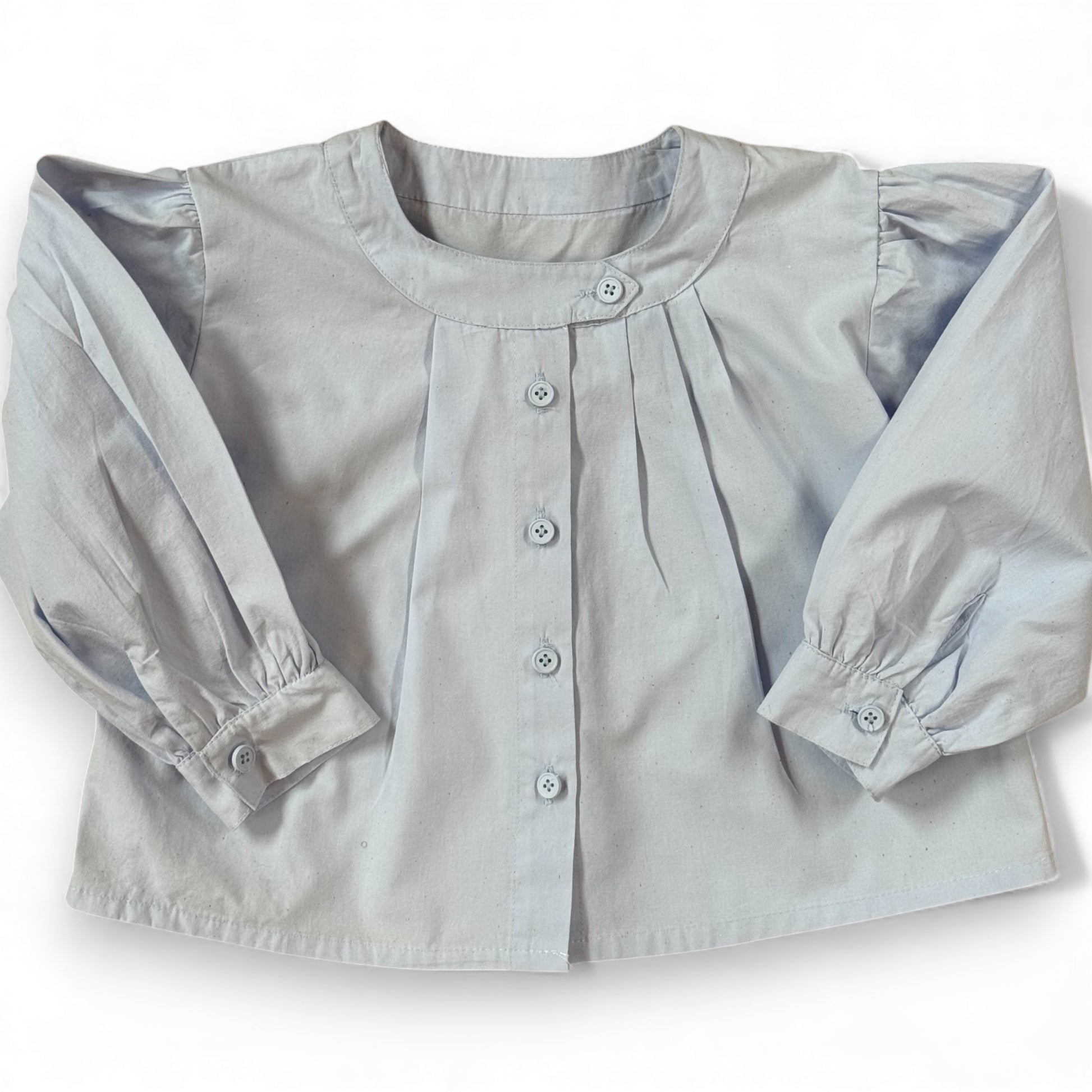 Children’s powder-blue A-line blouse with asymmetric band collar and off-centre pleats, laid flat.