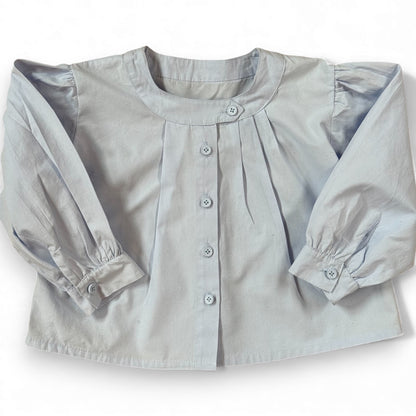 Children’s powder-blue A-line blouse with asymmetric band collar and off-centre pleats, laid flat.