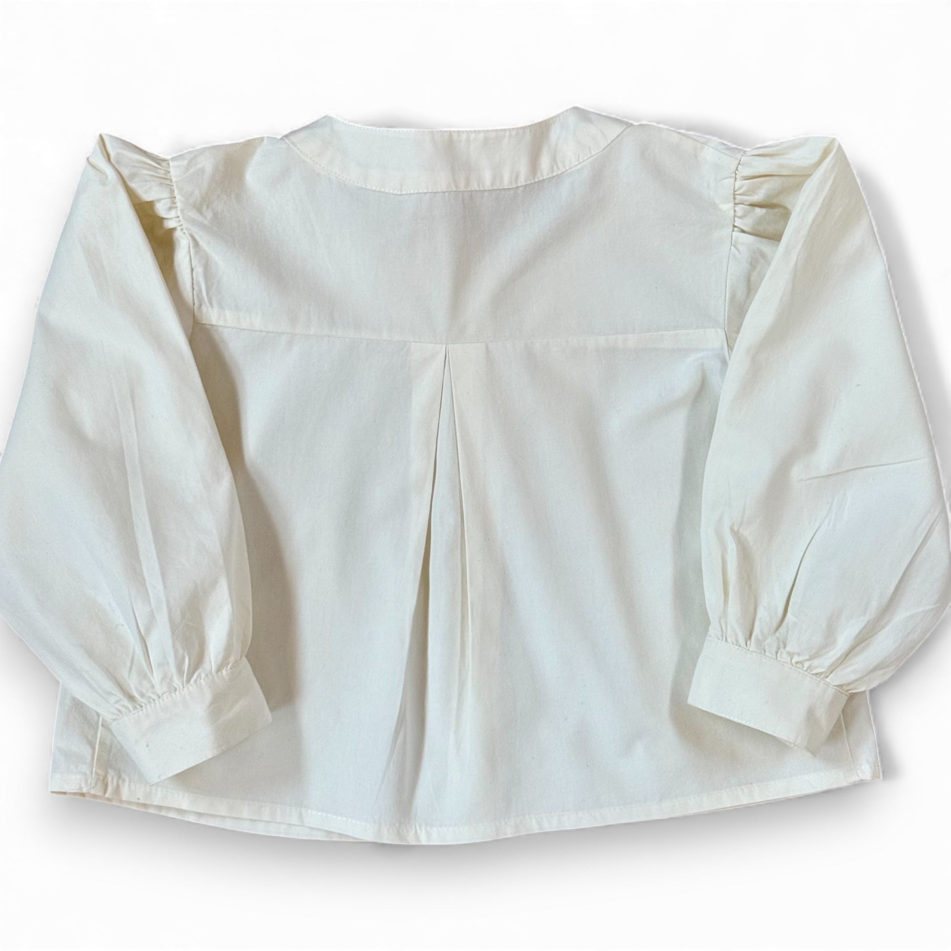 Back view of children’s white A-line blouse with centre back pleat and gathered sleeves, laid flat.”