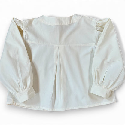 Back view of children’s white A-line blouse with centre back pleat and gathered sleeves, laid flat.”