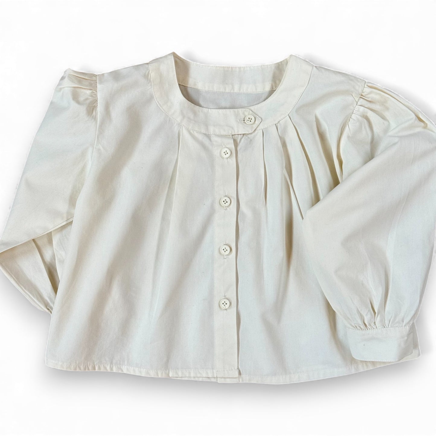 Children’s white A-line blouse with asymmetric band collar, off-centre pleats and drop shoulder, laid flat.