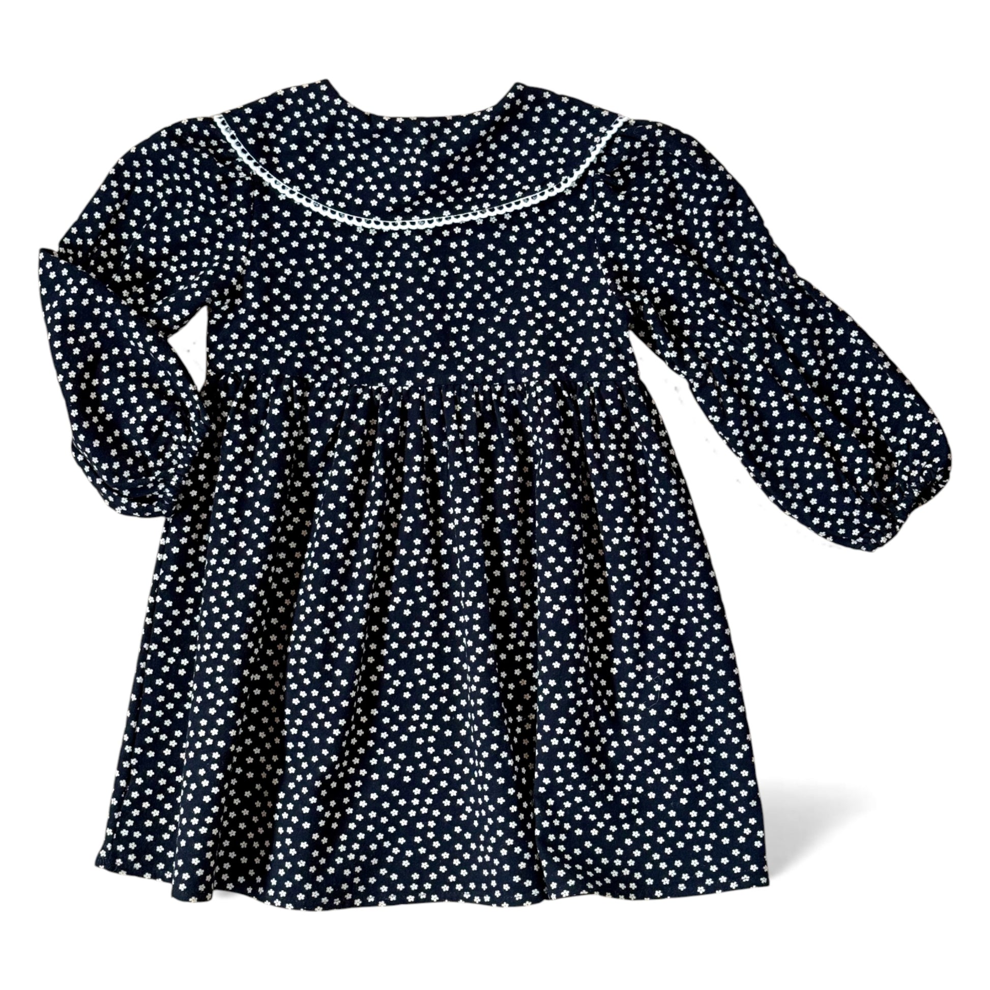 Navy brushed-cotton children’s dress with white micro-floral print, layered petal collar with contrast trim, long balloon sleeves with mid-arm and cuff elastic, empire line and gathered skirt — back view.