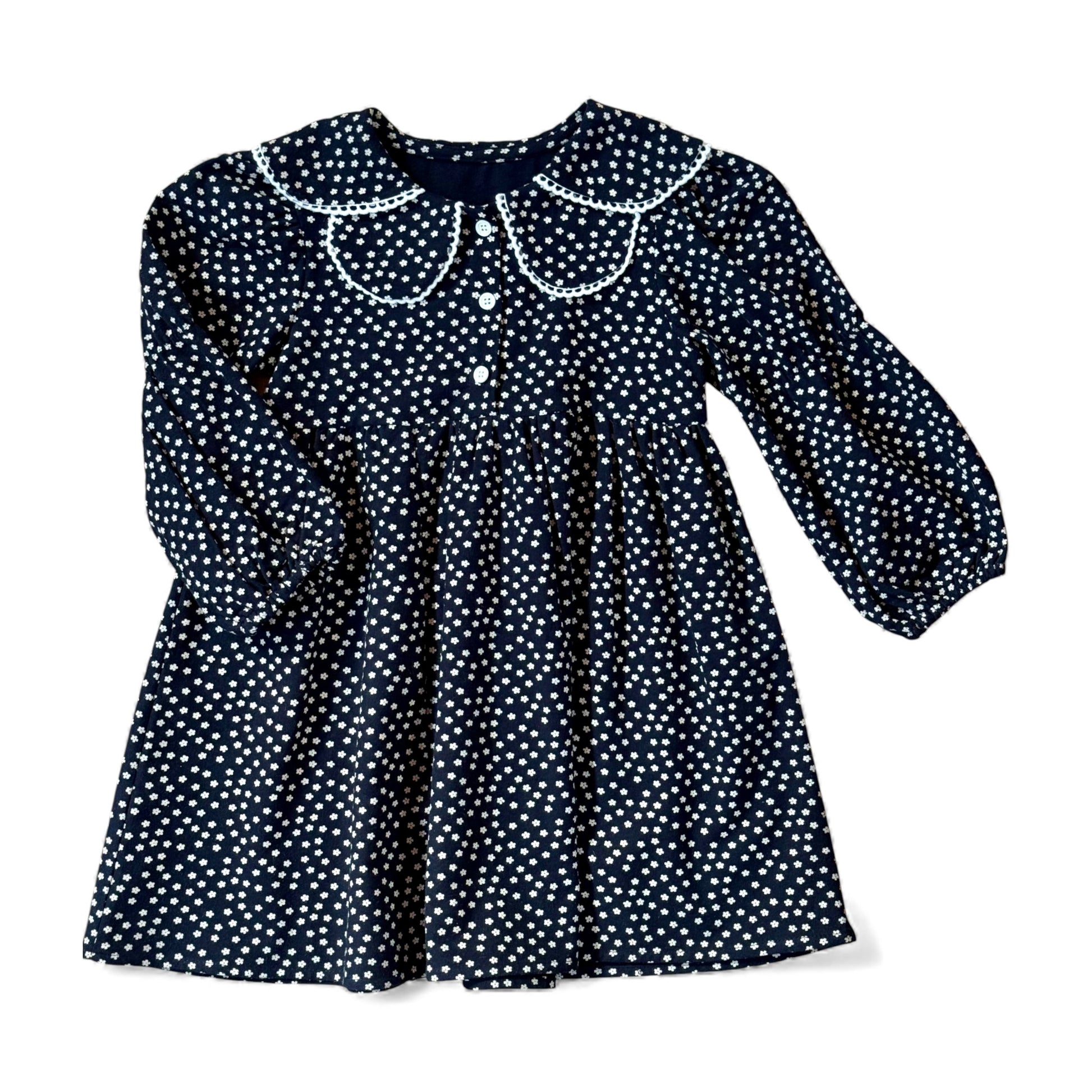 Navy brushed-cotton children’s dress with white micro-floral print, layered petal collar with contrast trim, long balloon sleeves with mid-arm and cuff elastic, empire line and gathered skirt — front view.